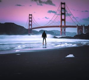 Rear view of man standing by sea during sunset