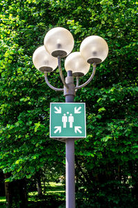 Sign board on lamp post against trees