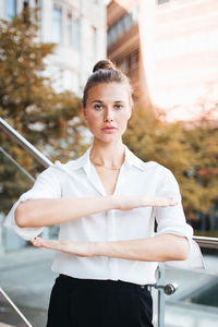 Portrait of young woman gesturing equality sign while standing in city