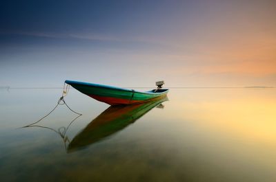 Boat moored at shore against sky during sunset