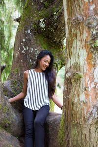 Happy young woman standing on tree trunk in forest