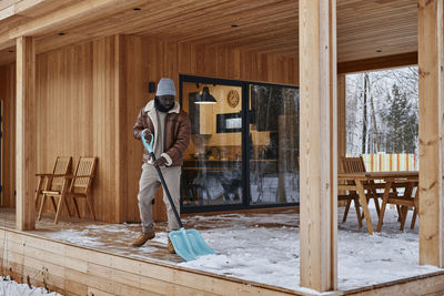 Man shoveling snow from porch outside house in winter