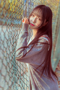 Portrait of young woman standing by chainlink fence