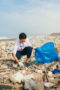 Vertical image of a latin woman volunteer picking up trash on a polluted beach.