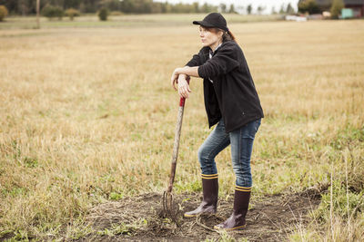 Full length of thoughtful woman with pitchfork standing at field