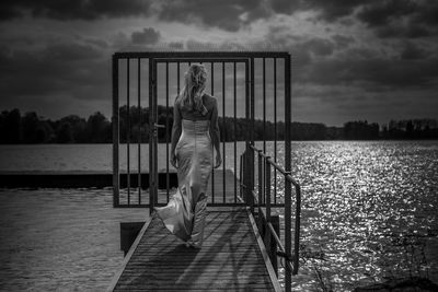 Rear view of woman walking on pier over lake against sky