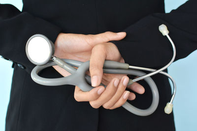 Midsection of doctor holding stethoscope while standing against blue background