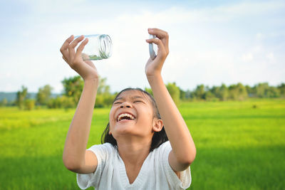 Laughing girl holding jar against field