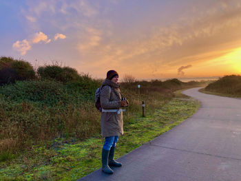 Rear view of man walking on road against sky during sunset