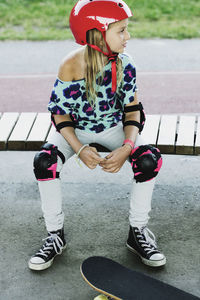 High angle view of girl wearing red helmet sitting on bench at skateboard park