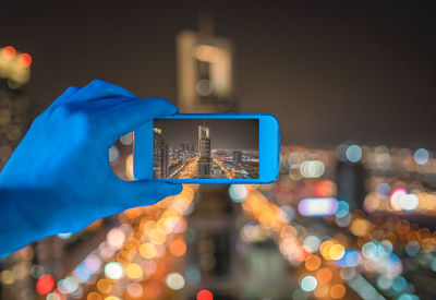 Man photographing illuminated cityscape with smart phone at night