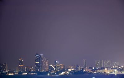 Illuminated modern buildings in city against sky at night