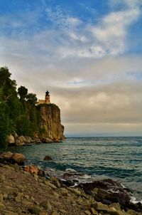 Lighthouse on rocks by sea against sky