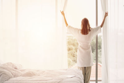 Rear view of woman with arms raised on bed