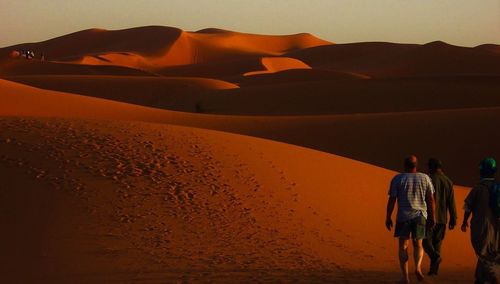 Rear view of people on desert against sky during sunset