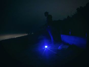 Silhouette people standing in illuminated dark against sky at night