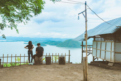 Rear view of men standing on railing against sky