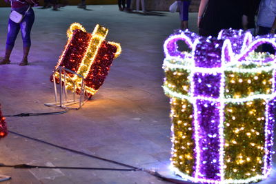 Low section of man standing by illuminated christmas lights at night