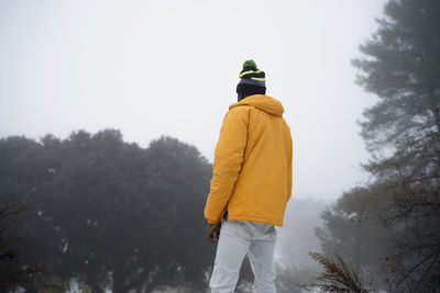 Back view of unrecognizable african american man with hands and pockets wearing outerwear standing in snowy park
