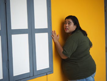 Overweight woman looking away while standing by wall