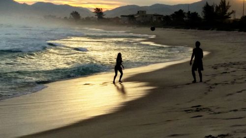 Silhouette people on beach against sky during sunset