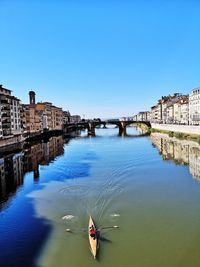 High angle view of man kayaking in river amidst buildings in city against sky during sunny day