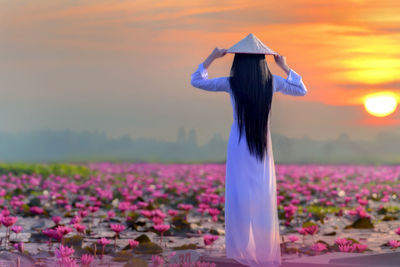 Woman standing on field against sky during sunset