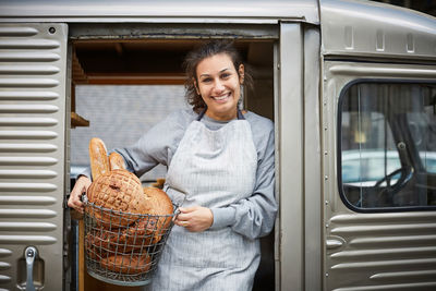 Smiling saleswoman carrying basket of fresh breads in food truck