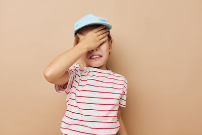 Girl covering eyes while standing against beige background