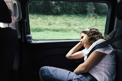 Bored girl looking through window while sitting in car