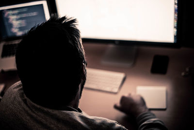 Rear view of man using computer while sitting on table at home