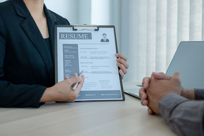 Midsection of female manager showing resume to candidate at desk