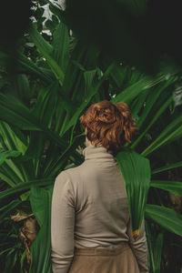 A beautiful plus size girl with red hair among the lush green branches of tropical plants. 