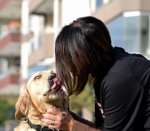 Close-up of dog licking woman sitting against building 