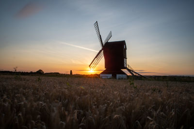 Traditional windmill on field against sky during sunset