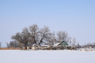 House on snow covered field against clear blue sky