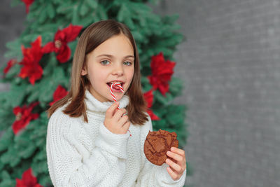 Young girl in white knitted sweater smiling and eating christmas cookie