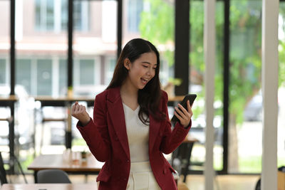 Young woman using smart phone while standing on laptop