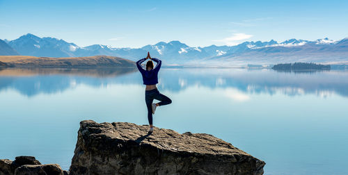 Man standing on rock by lake against sky