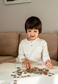 Happy little child counting coins putting them into glass jar. kid counting money saving from change 