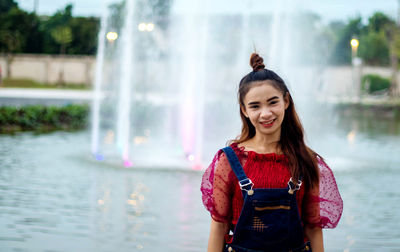 Portrait of smiling young woman standing against fountain