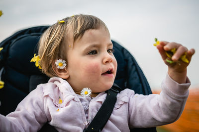 Close up portrait of little curious child with blond hair watching flowers in her hand