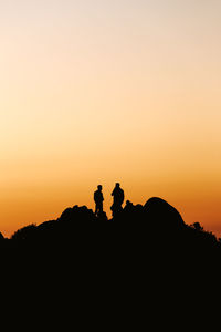 Silhouette people on rock against sky during sunset