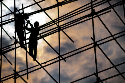 Low angle view worker standing on scaffolding against sky during sunset