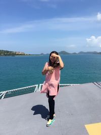 Portrait of smiling woman standing on pier against sky