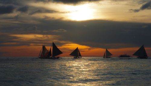 Boats sailing on sea against cloudy sky during sunset