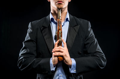 Midsection of man holding gun while standing against black background