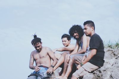 Friends sitting on rock against sky