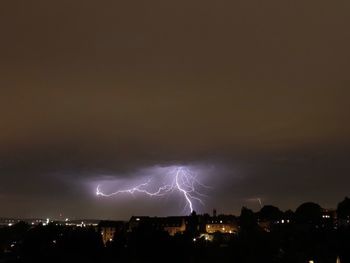 Lightning over illuminated cityscape against dramatic sky at night
