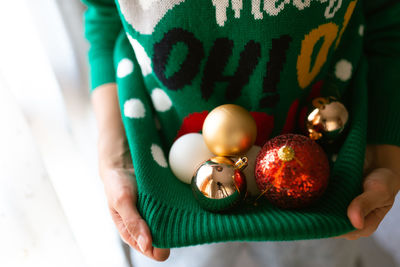 Midsection of woman carrying christmas ornament in sweater